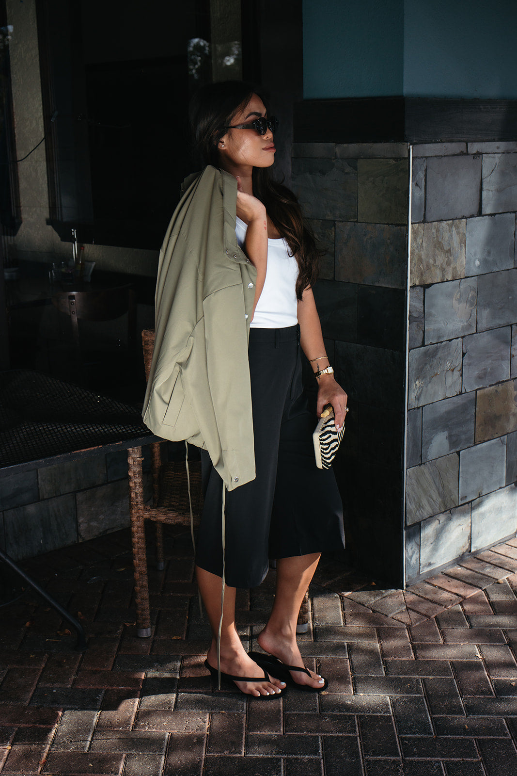 Woman wearing the Naia Funnel Neck Jacket, a lightweight light olive snap-front jacket with a drawstring hem