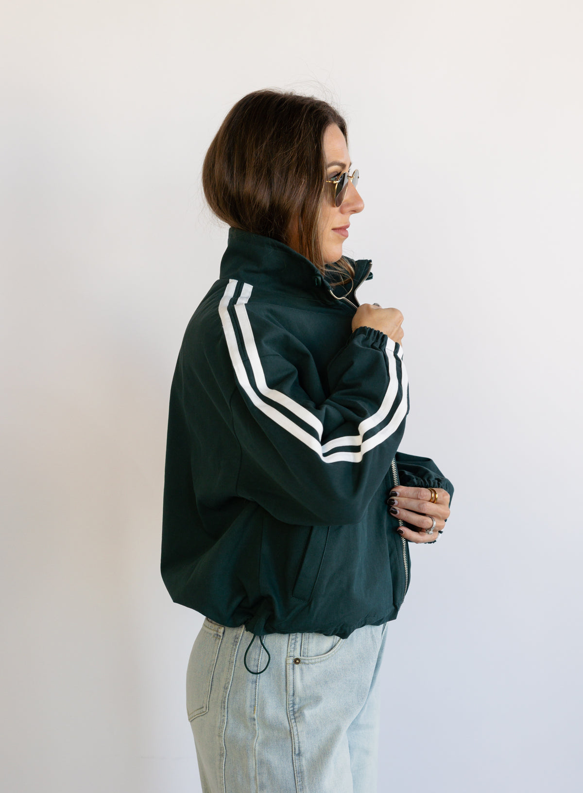 Woman wearing the Marina Twill Track Jacket, a forest green zip-up jacket with white sleeve stripes