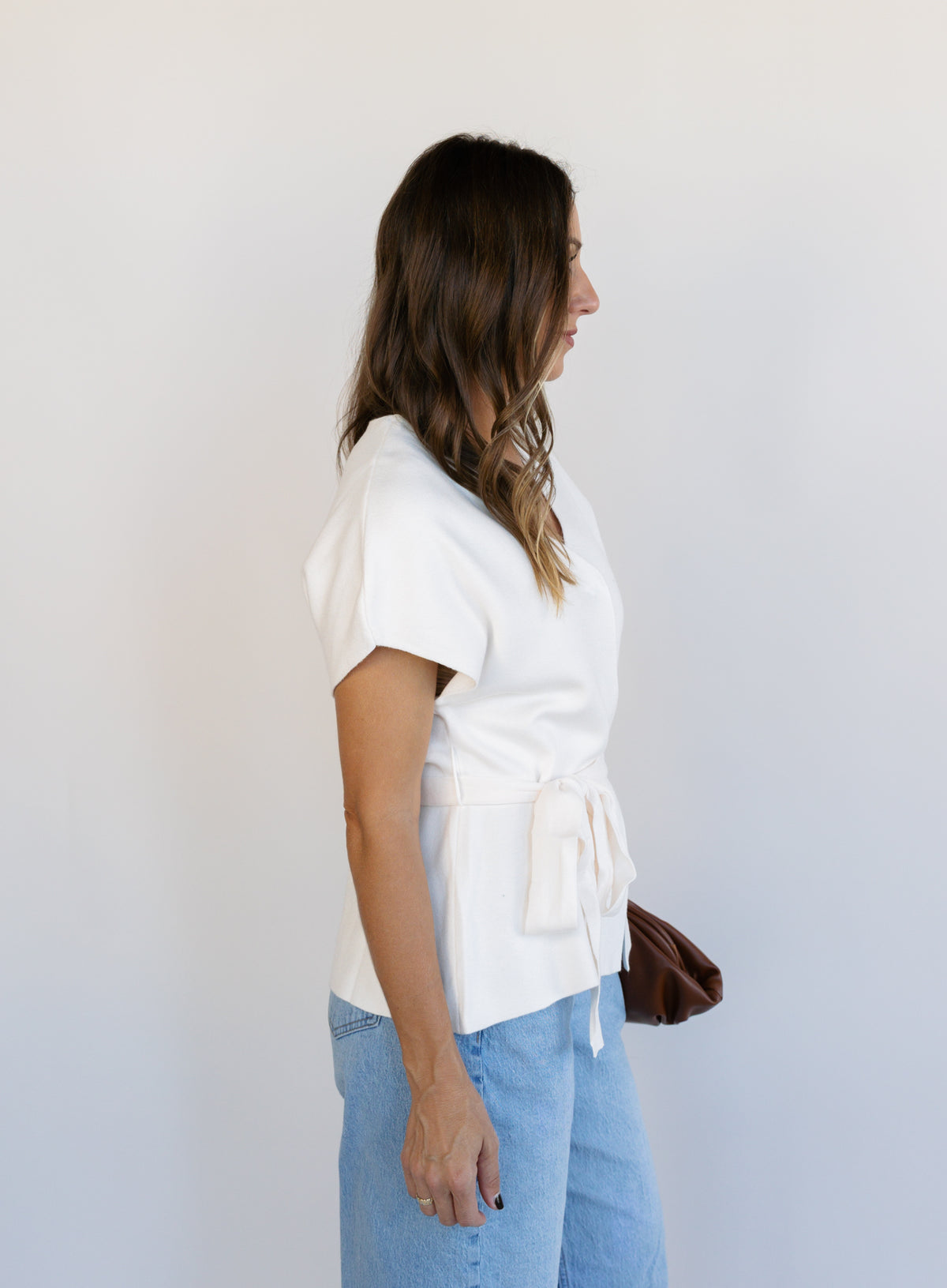Woman wearing the Yara Belted Top, an ivory V-neck knit top with a detachable belt