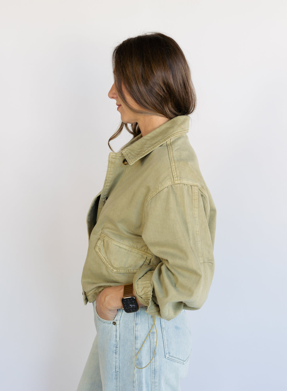 Woman wearing the Zuri Denim Jacket, a light olive cropped cotton twill utility jacket