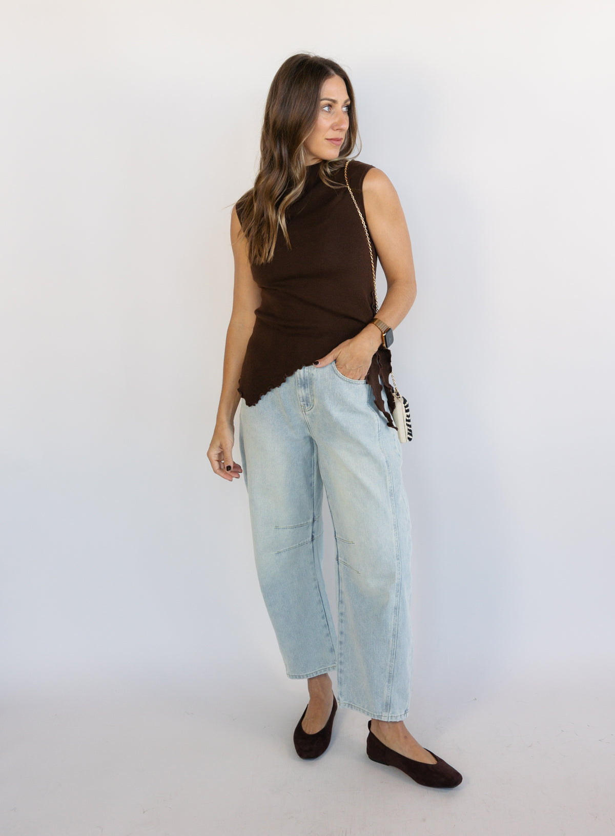 Woman wearing the Coralie Ruffle Trim Sweater Tank, a chocolate brown mock neck knit tank with a ruffle hem
