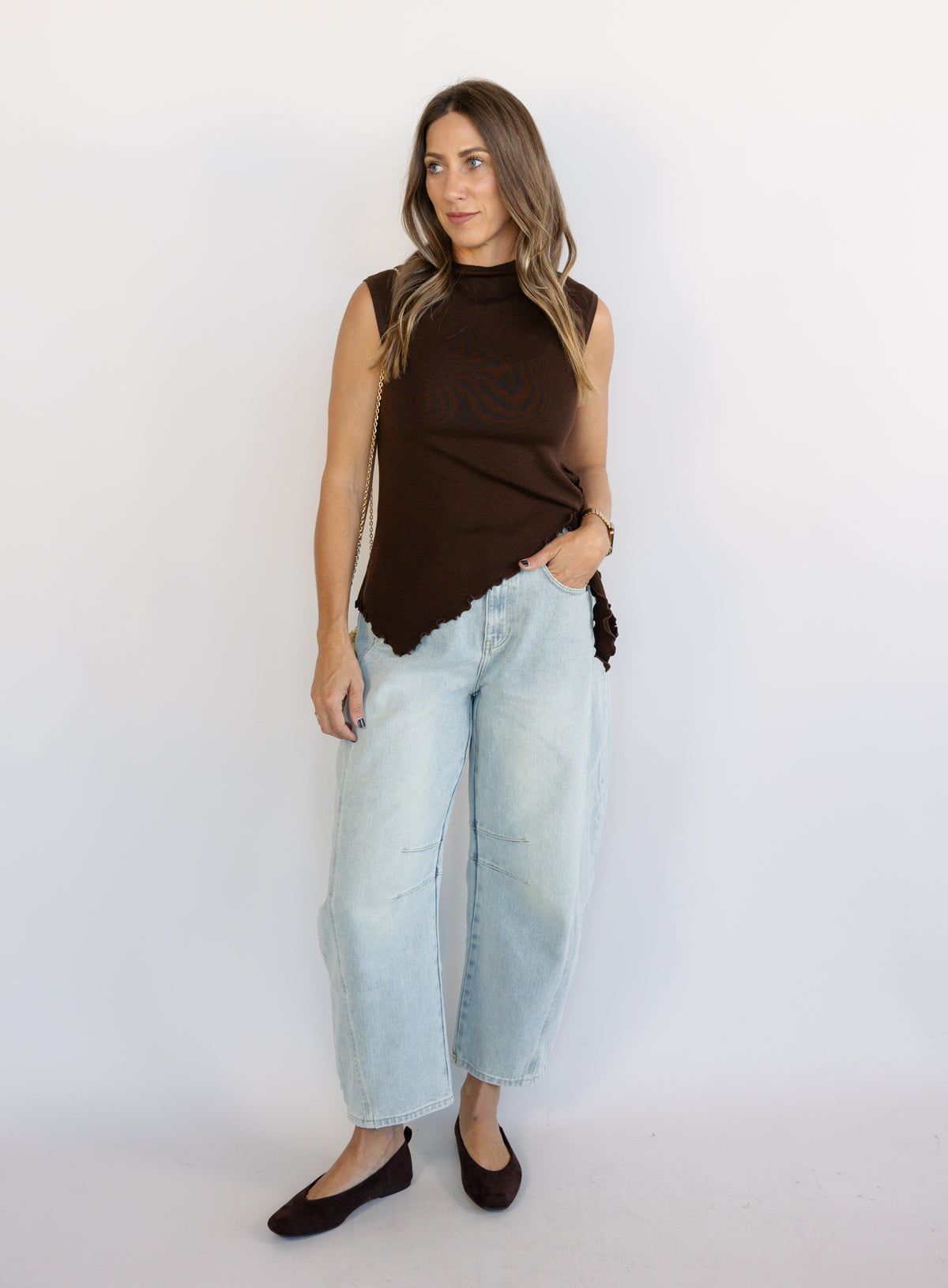 Woman wearing the Coralie Ruffle Trim Sweater Tank, a chocolate brown mock neck knit tank with a ruffle hem