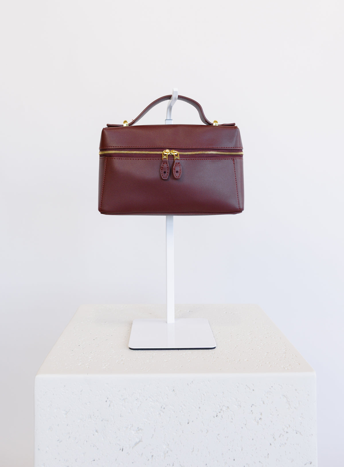 Sabine Bag, a burgundy boxy top-handle bag with gold hardware and a crossbody strap