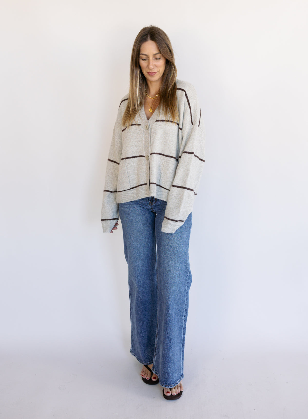 Woman wearing the Juno Striped Knit Cardigan, a mushroom knit cardigan with chocolate stripes and a V-neck