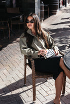 Woman wearing the Naia Funnel Neck Jacket, a lightweight light olive snap-front jacket with a drawstring hem