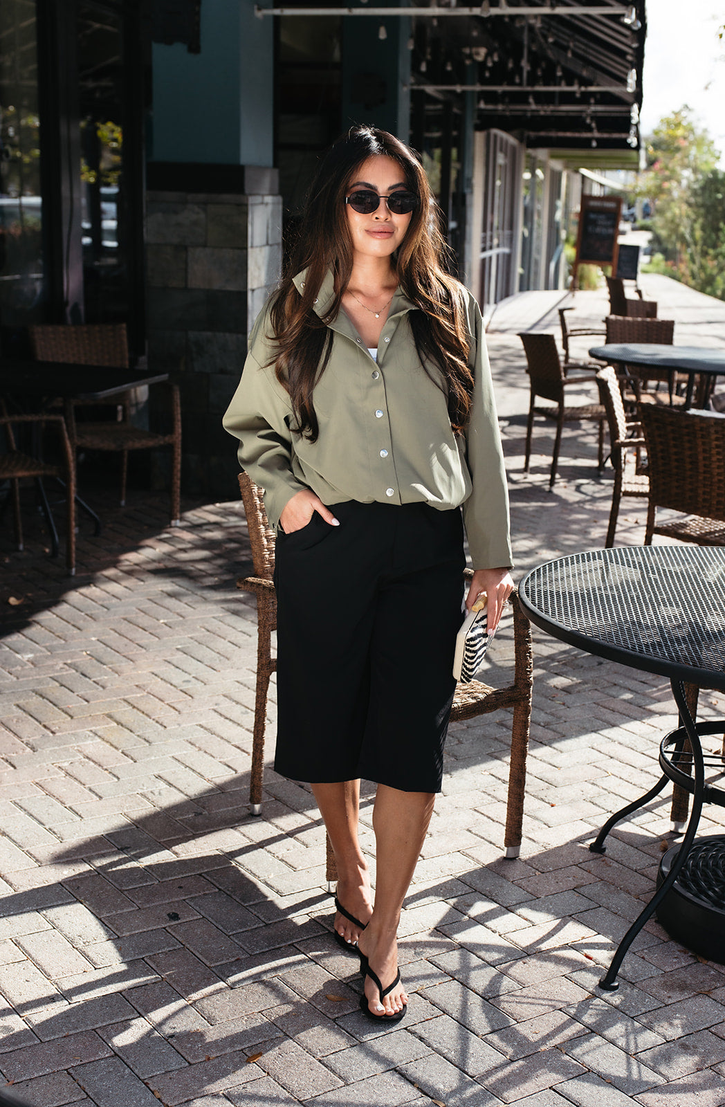 Woman wearing the Naia Funnel Neck Jacket, a lightweight light olive snap-front jacket with a drawstring hem