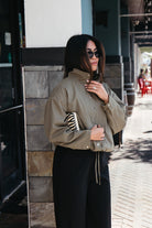 Woman wearing the Naia Funnel Neck Jacket, a lightweight light olive snap-front jacket with a drawstring hem