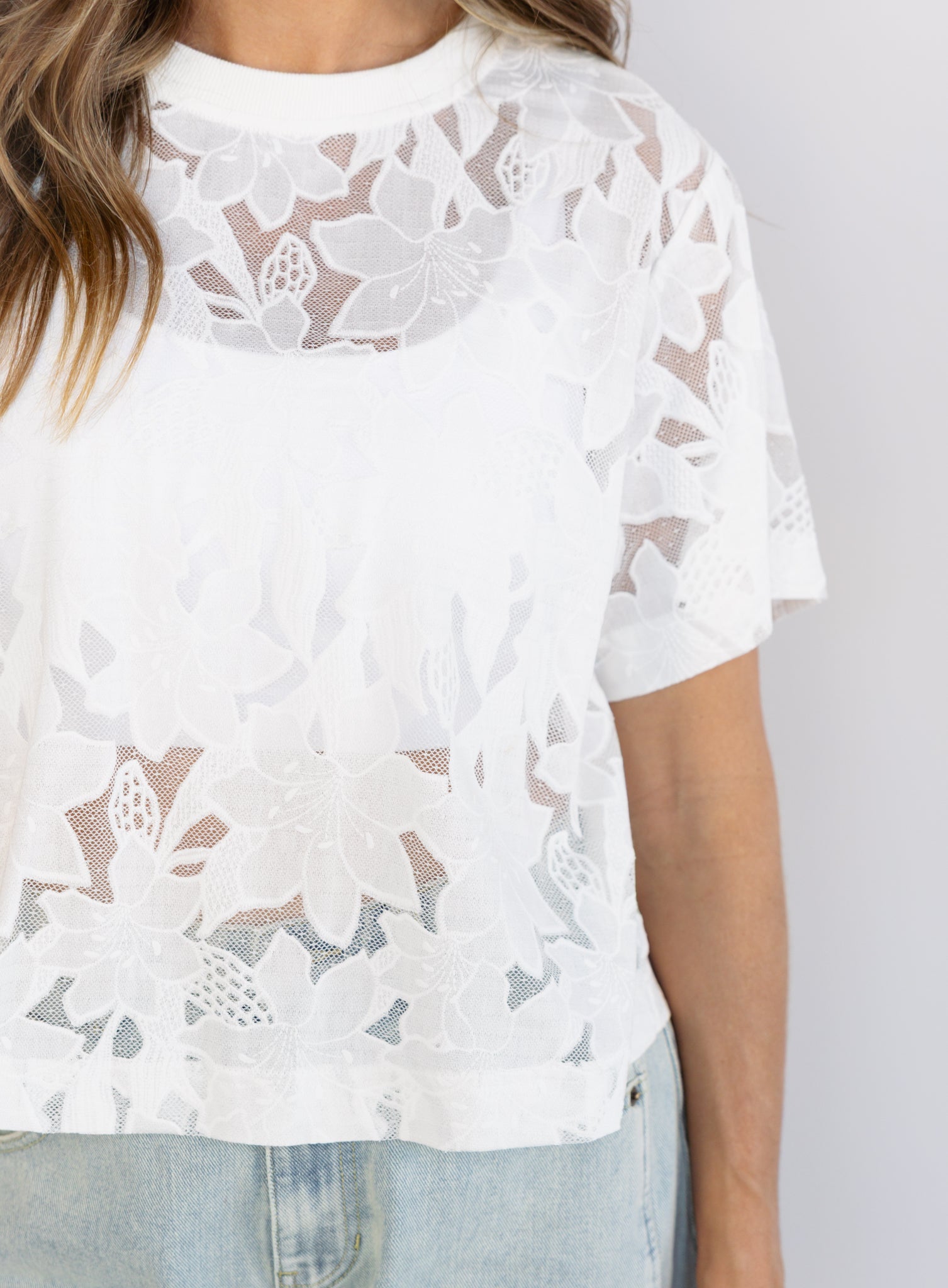 Woman wearing the Lillia Lace Floral Tee, a sheer white mesh tee with floral embroidery