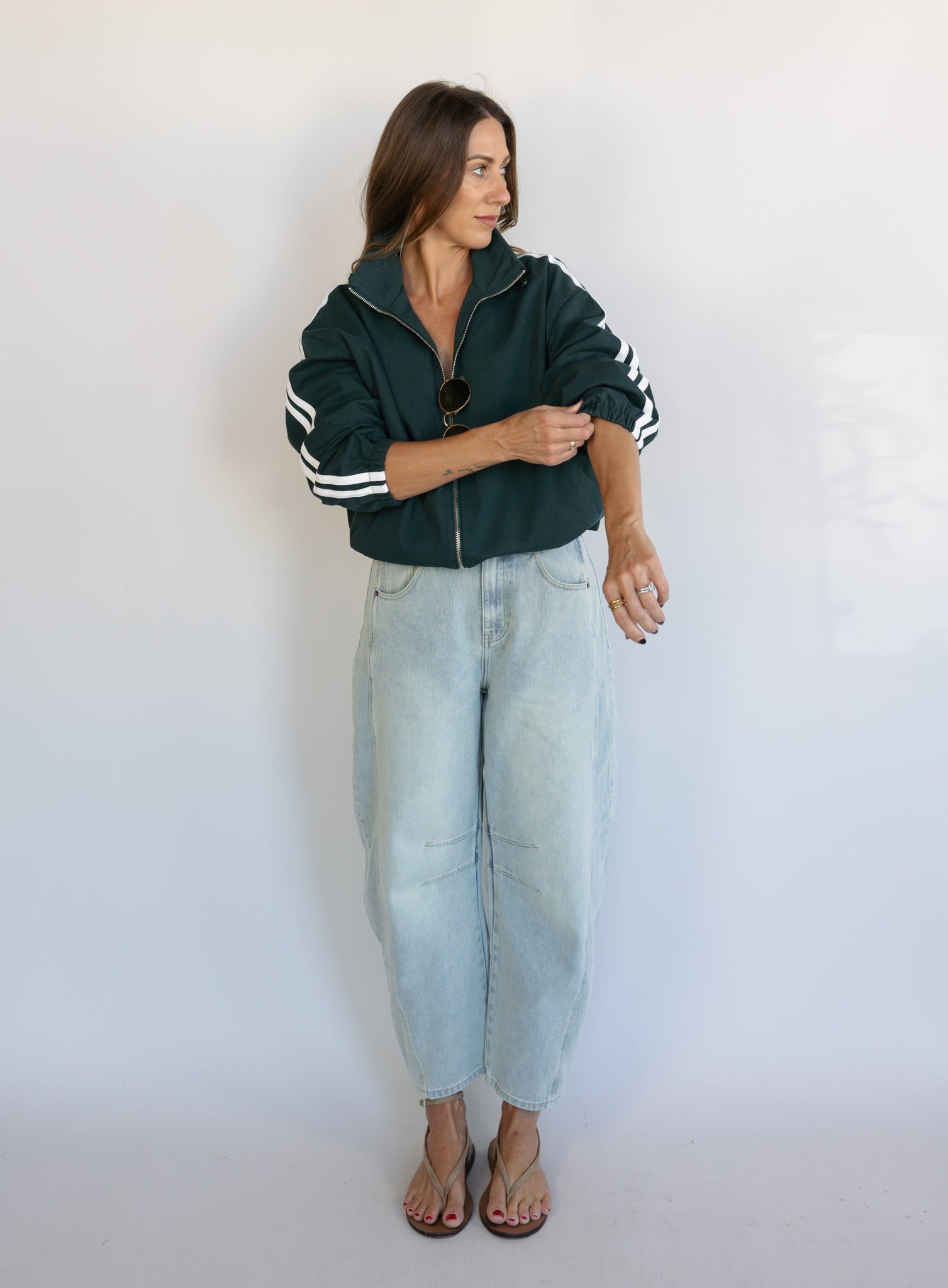Woman wearing the Marina Twill Track Jacket, a forest green zip-up jacket with white sleeve stripes