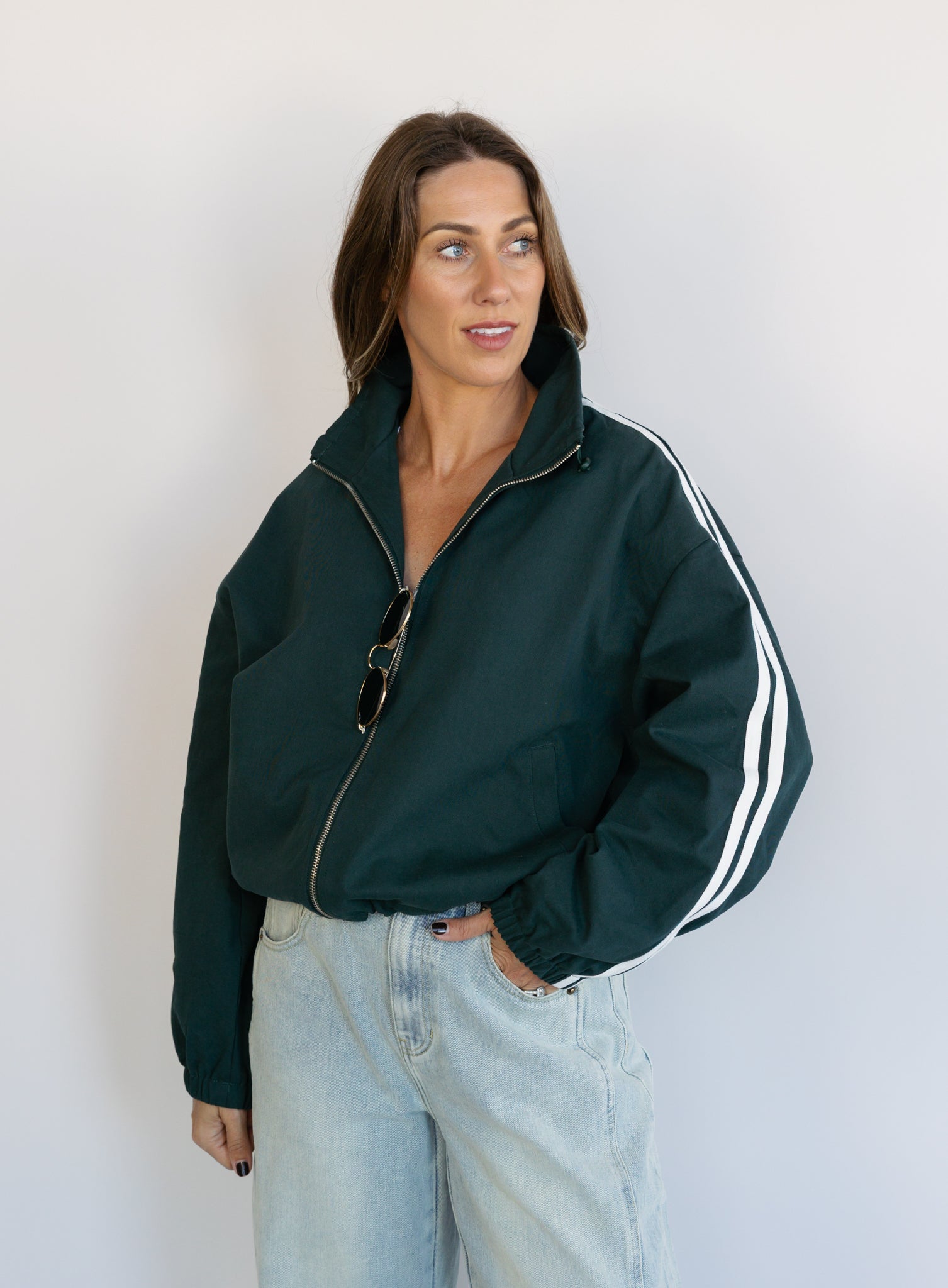 Woman wearing the Marina Twill Track Jacket, a forest green zip-up jacket with white sleeve stripes