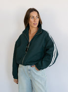 Woman wearing the Marina Twill Track Jacket, a forest green zip-up jacket with white sleeve stripes