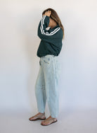 Woman wearing the Marina Twill Track Jacket, a forest green zip-up jacket with white sleeve stripes