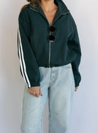 Woman wearing the Marina Twill Track Jacket, a forest green zip-up jacket with white sleeve stripes