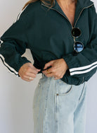 Woman wearing the Marina Twill Track Jacket, a forest green zip-up jacket with white sleeve stripes