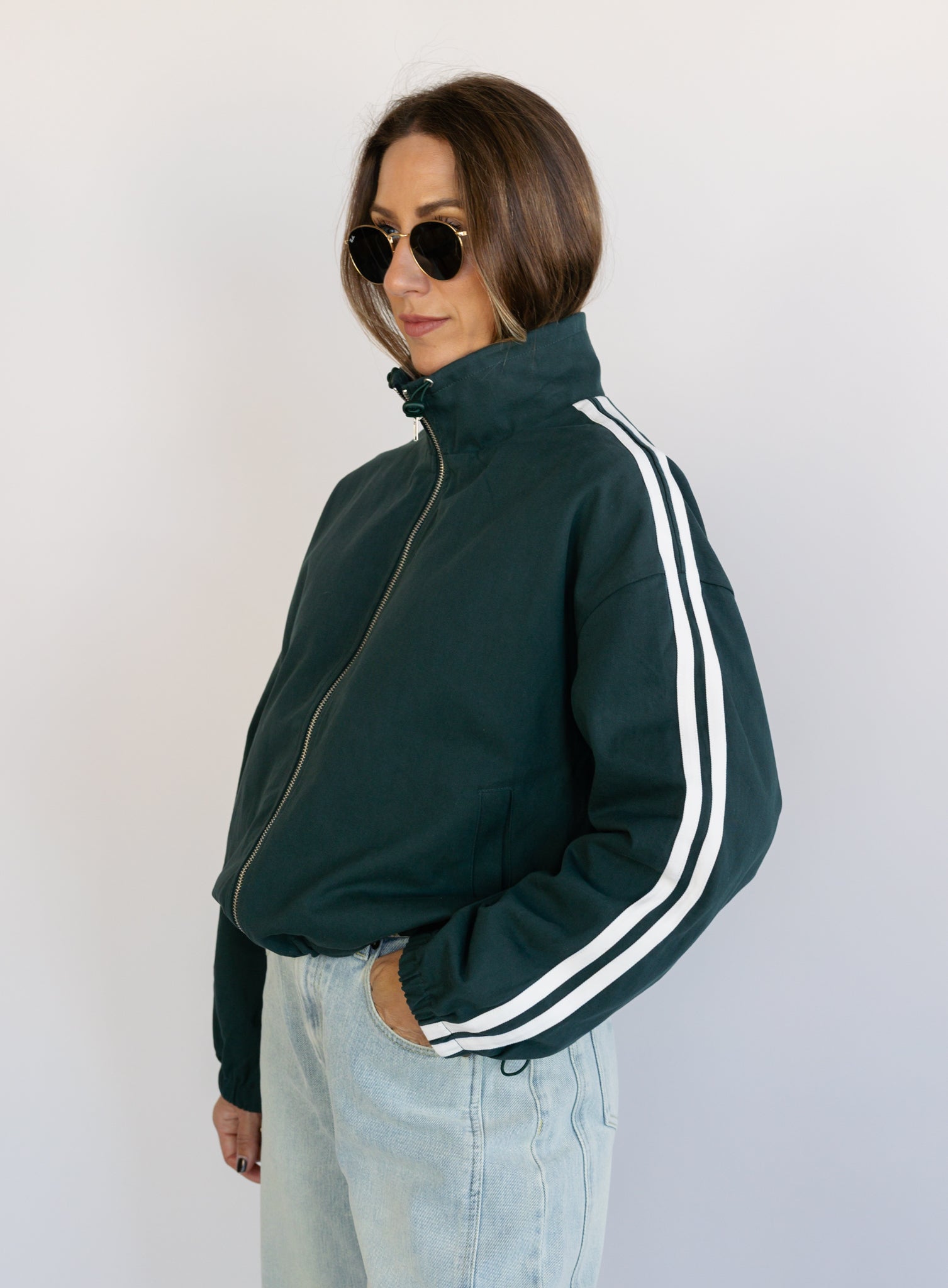 Woman wearing the Marina Twill Track Jacket, a forest green zip-up jacket with white sleeve stripes
