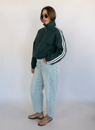 Woman wearing the Marina Twill Track Jacket, a forest green zip-up jacket with white sleeve stripes