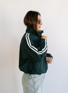 Woman wearing the Marina Twill Track Jacket, a forest green zip-up jacket with white sleeve stripes