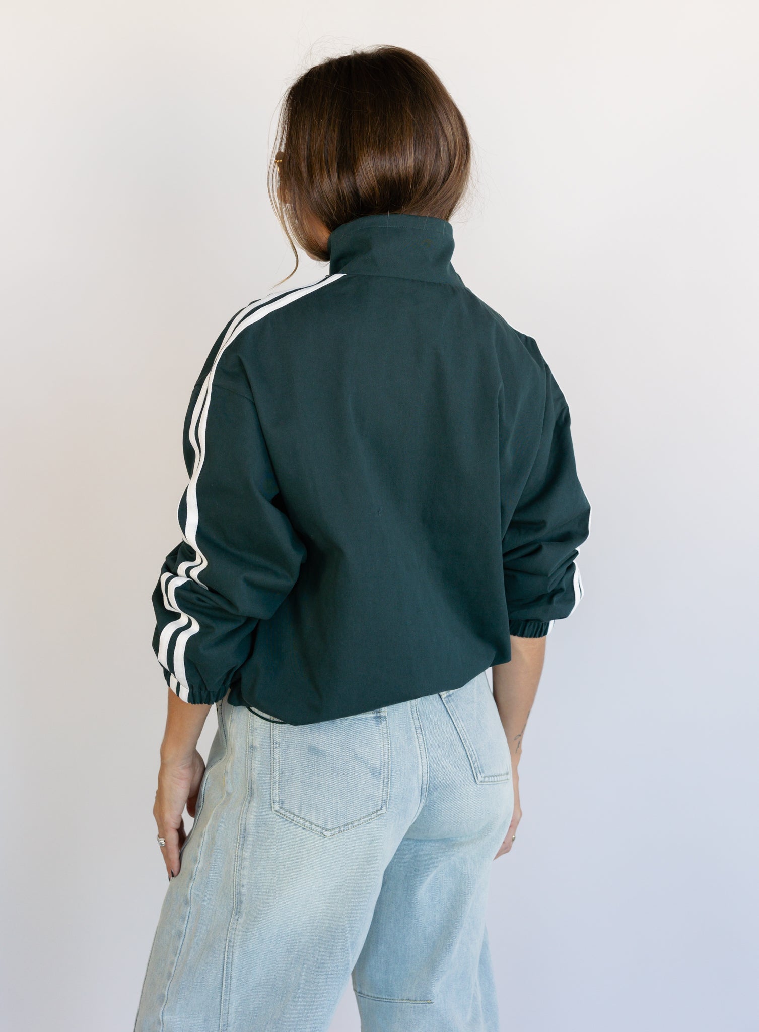 Woman wearing the Marina Twill Track Jacket, a forest green zip-up jacket with white sleeve stripes