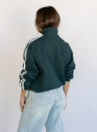 Woman wearing the Marina Twill Track Jacket, a forest green zip-up jacket with white sleeve stripes