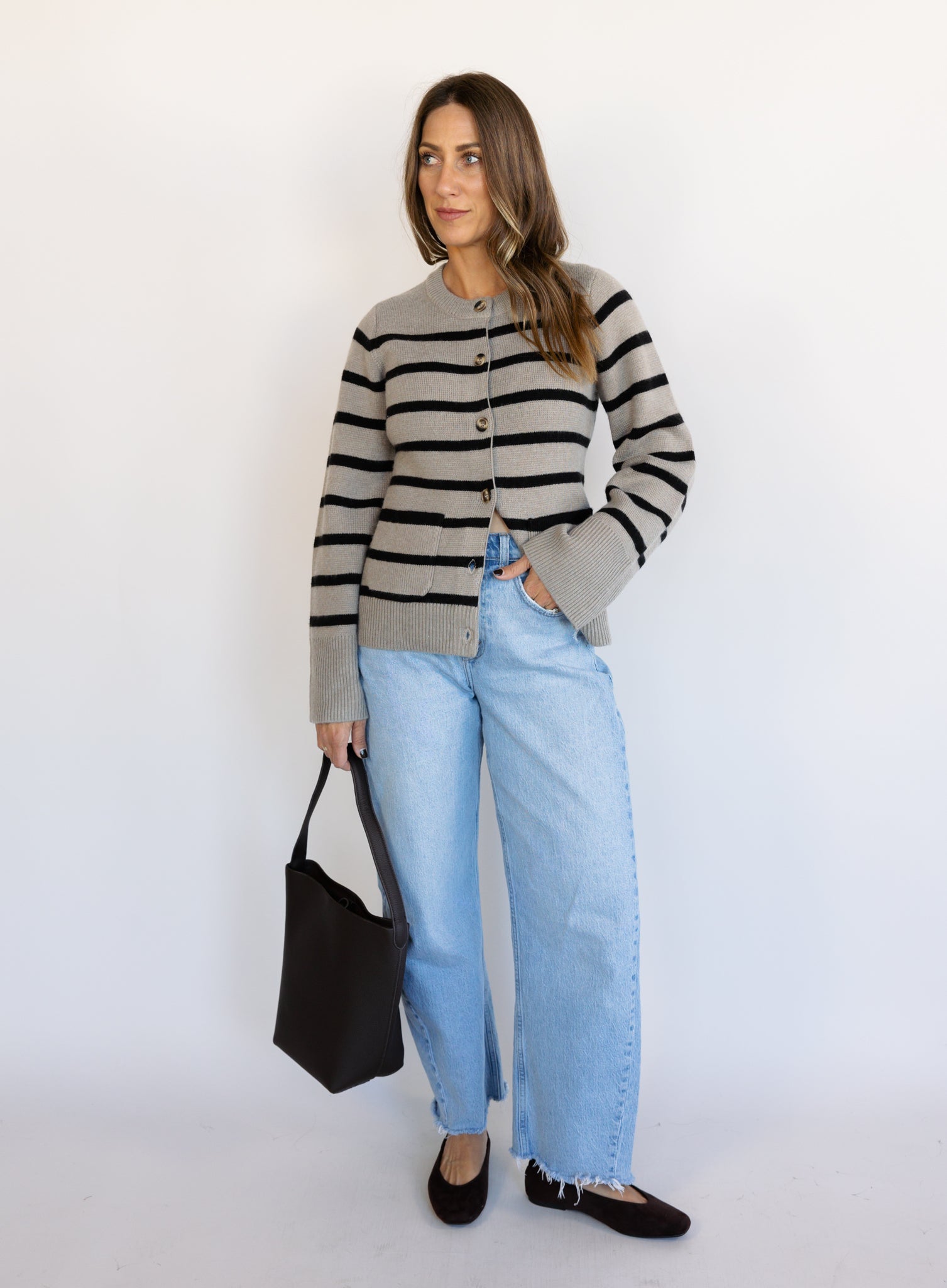 Woman wearing the Hannah Stripe Knit Cardigan, a greige and black striped button-front cardigan