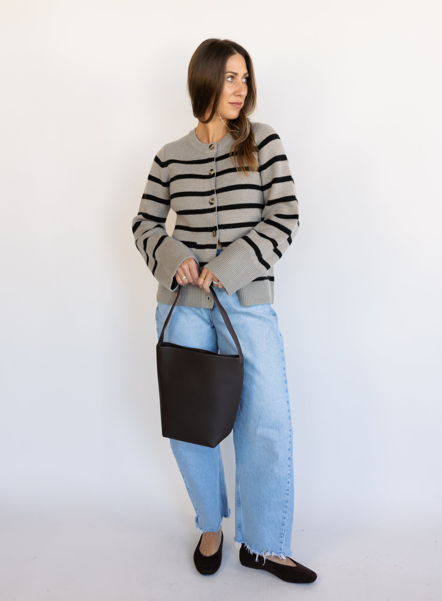 Woman wearing the Hannah Stripe Knit Cardigan, a greige and black striped button-front cardigan