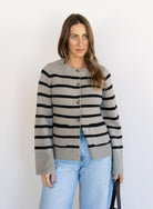Woman wearing the Hannah Stripe Knit Cardigan, a greige and black striped button-front cardigan