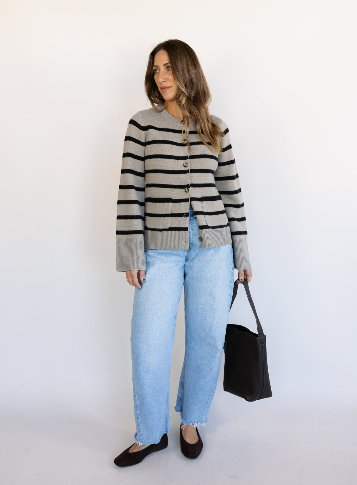 Woman wearing the Hannah Stripe Knit Cardigan, a greige and black striped button-front cardigan