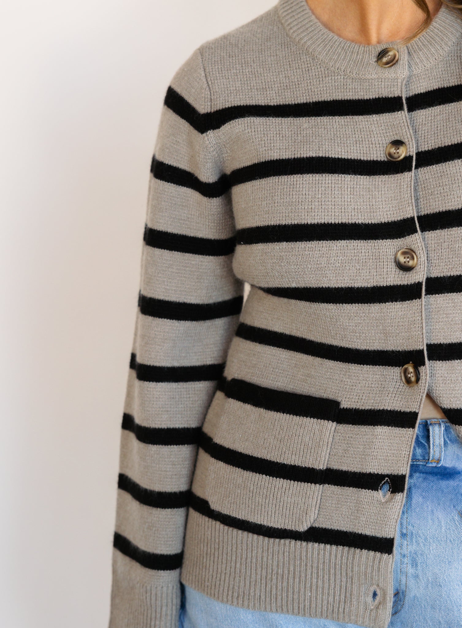 Woman wearing the Hannah Stripe Knit Cardigan, a greige and black striped button-front cardigan