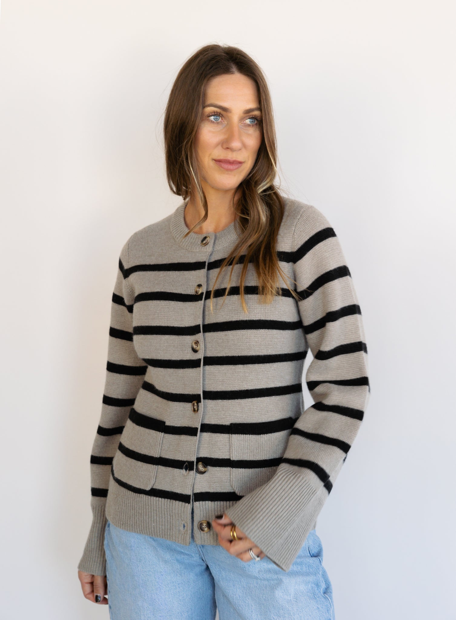 Woman wearing the Hannah Stripe Knit Cardigan, a greige and black striped button-front cardigan