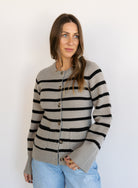 Woman wearing the Hannah Stripe Knit Cardigan, a greige and black striped button-front cardigan