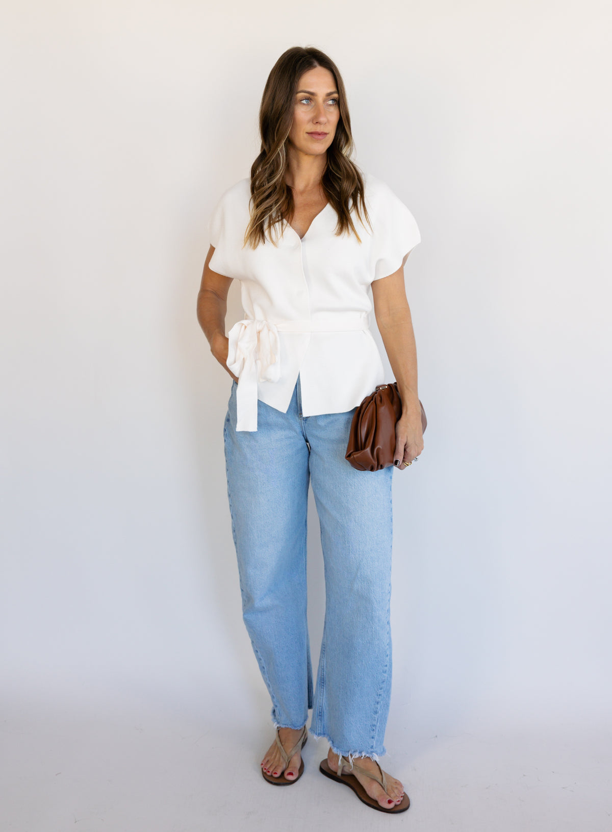 Woman wearing the Yara Belted Top, an ivory V-neck knit top with a detachable belt