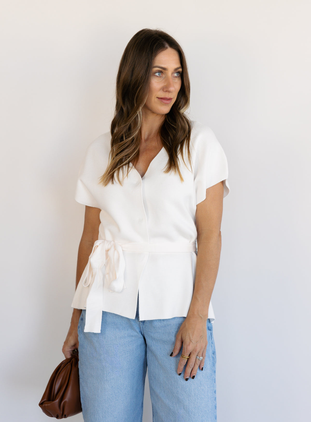 Woman wearing the Yara Belted Top, an ivory V-neck knit top with a detachable belt