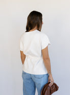 Woman wearing the Yara Belted Top, an ivory V-neck knit top with a detachable belt