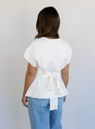 Woman wearing the Yara Belted Top, an ivory V-neck knit top with a detachable belt