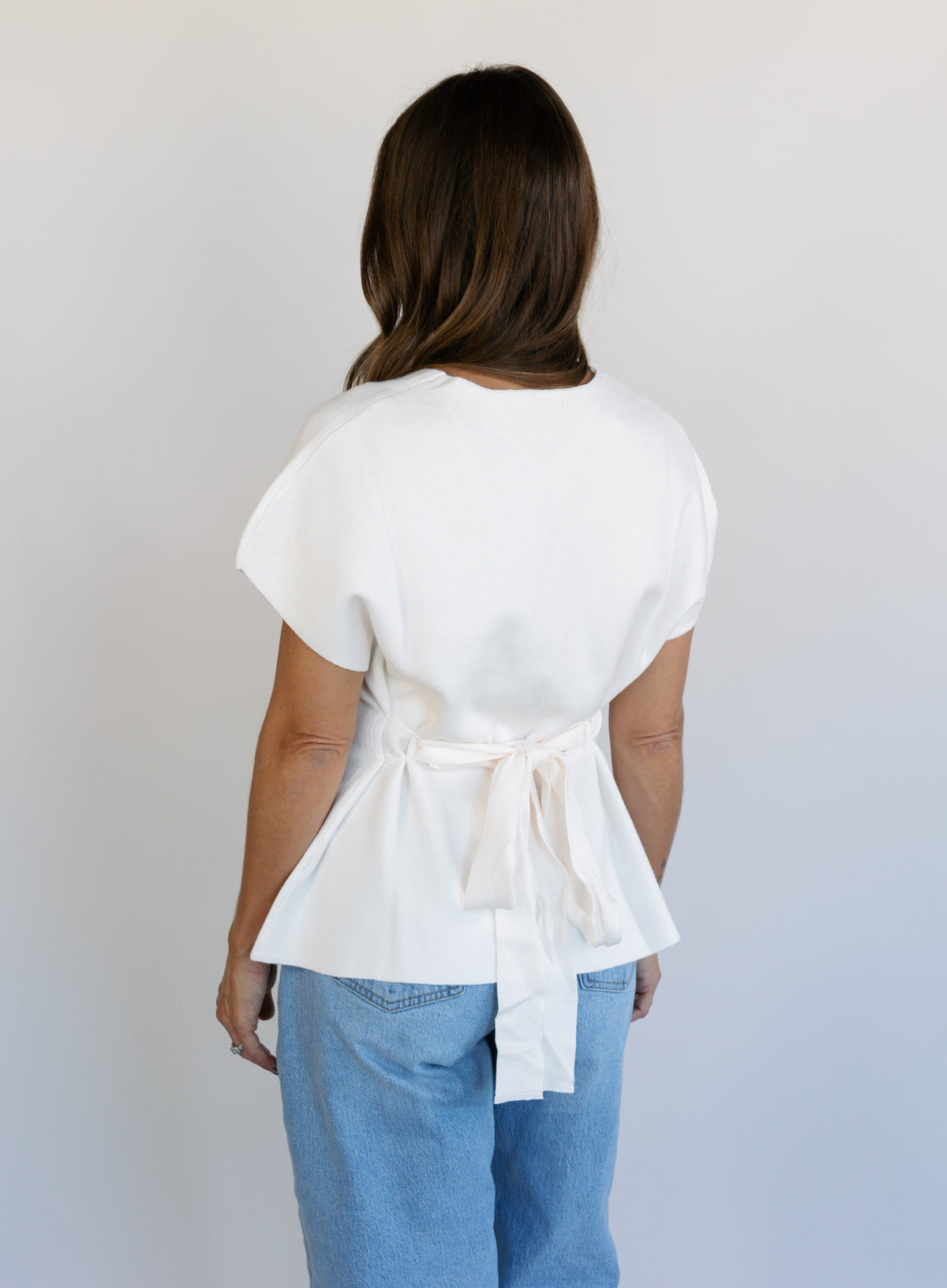 Woman wearing the Yara Belted Top, an ivory V-neck knit top with a detachable belt