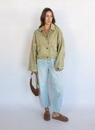 Woman wearing the Zuri Denim Jacket, a light olive cropped cotton twill utility jacket