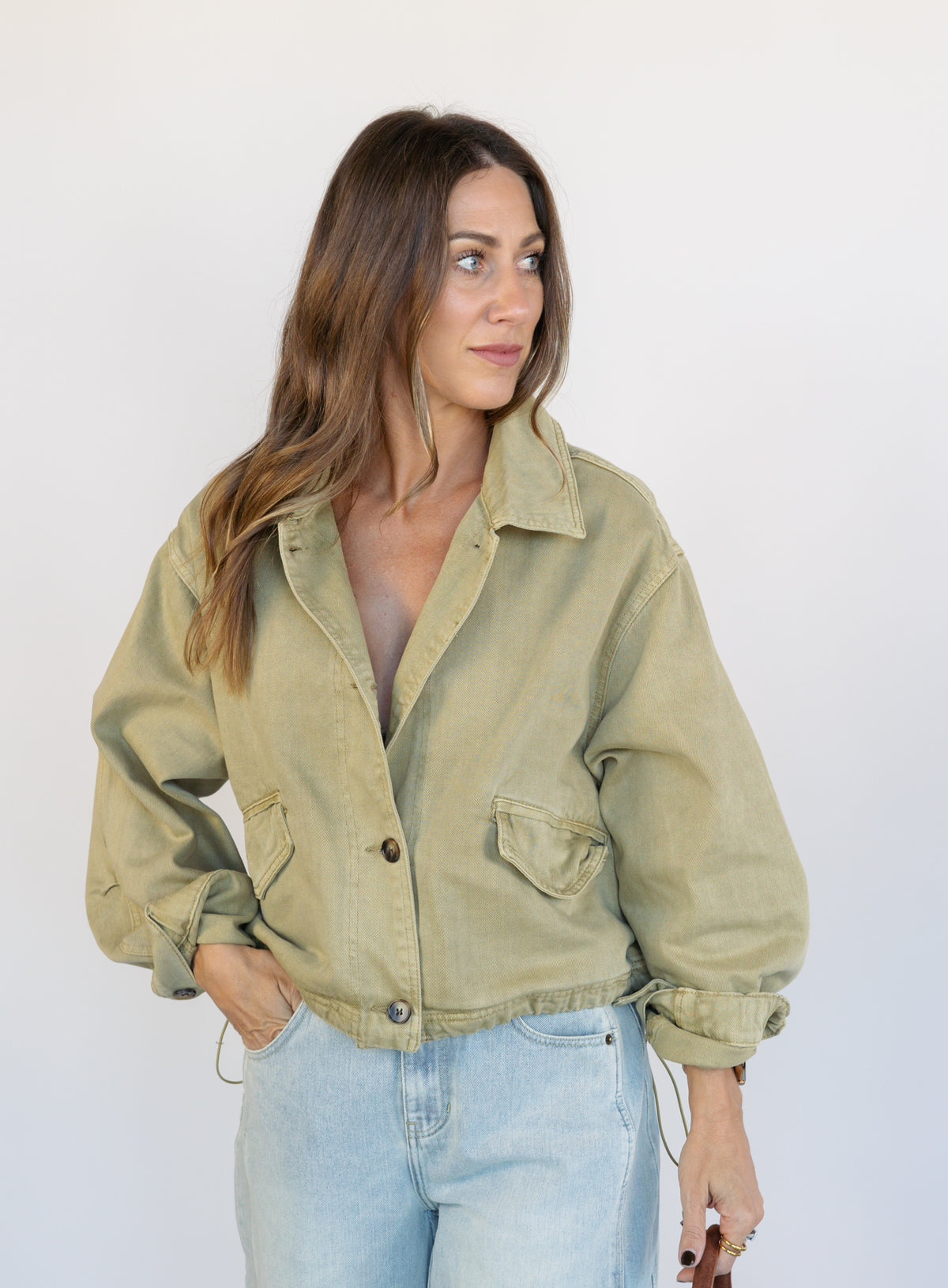 Woman wearing the Zuri Denim Jacket, a light olive cropped cotton twill utility jacket