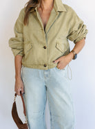 Woman wearing the Zuri Denim Jacket, a light olive cropped cotton twill utility jacket