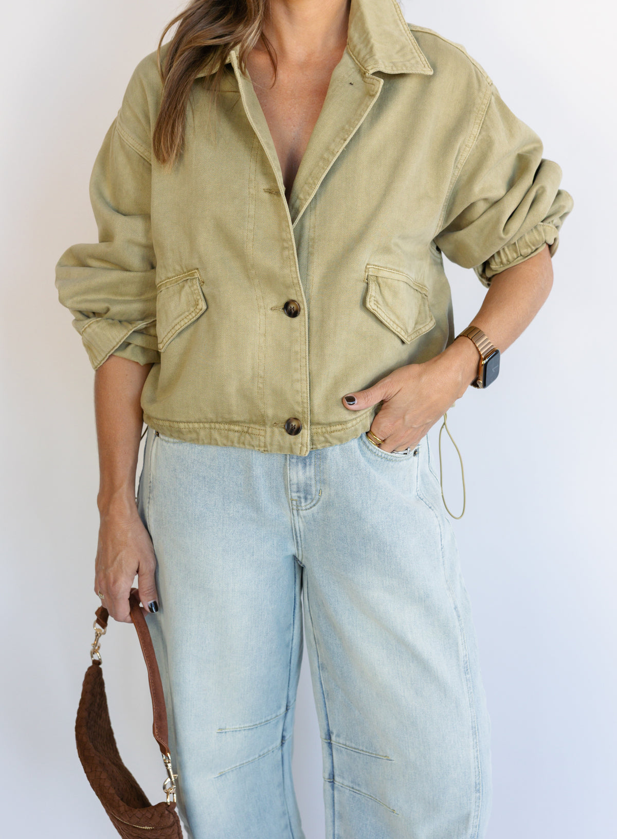 Woman wearing the Zuri Denim Jacket, a light olive cropped cotton twill utility jacket