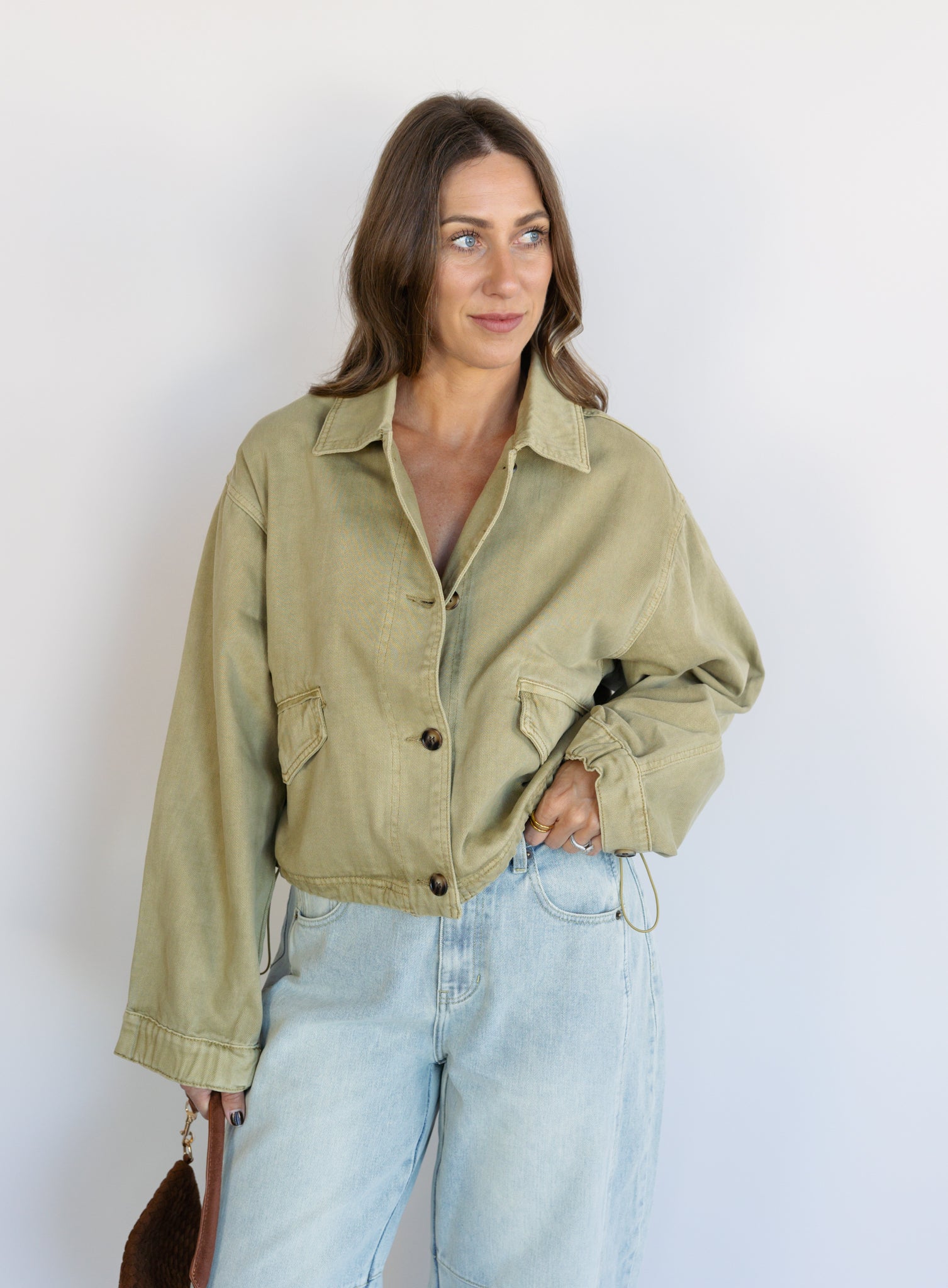 Woman wearing the Zuri Denim Jacket, a light olive cropped cotton twill utility jacket
