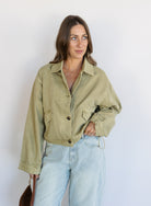 Woman wearing the Zuri Denim Jacket, a light olive cropped cotton twill utility jacket