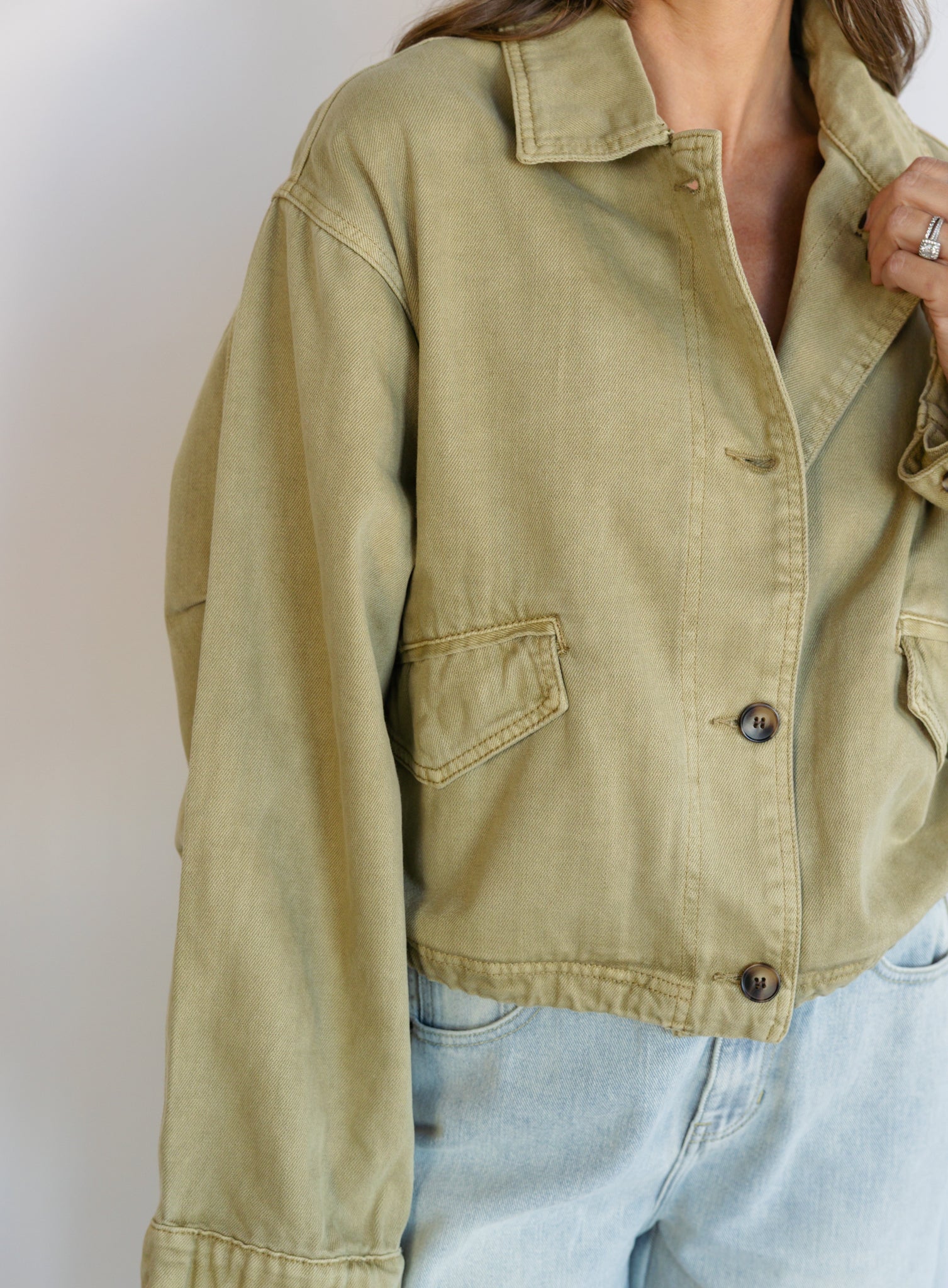 Woman wearing the Zuri Denim Jacket, a light olive cropped cotton twill utility jacket