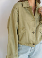 Woman wearing the Zuri Denim Jacket, a light olive cropped cotton twill utility jacket