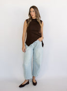 Woman wearing the Coralie Ruffle Trim Sweater Tank, a chocolate brown mock neck knit tank with a ruffle hem