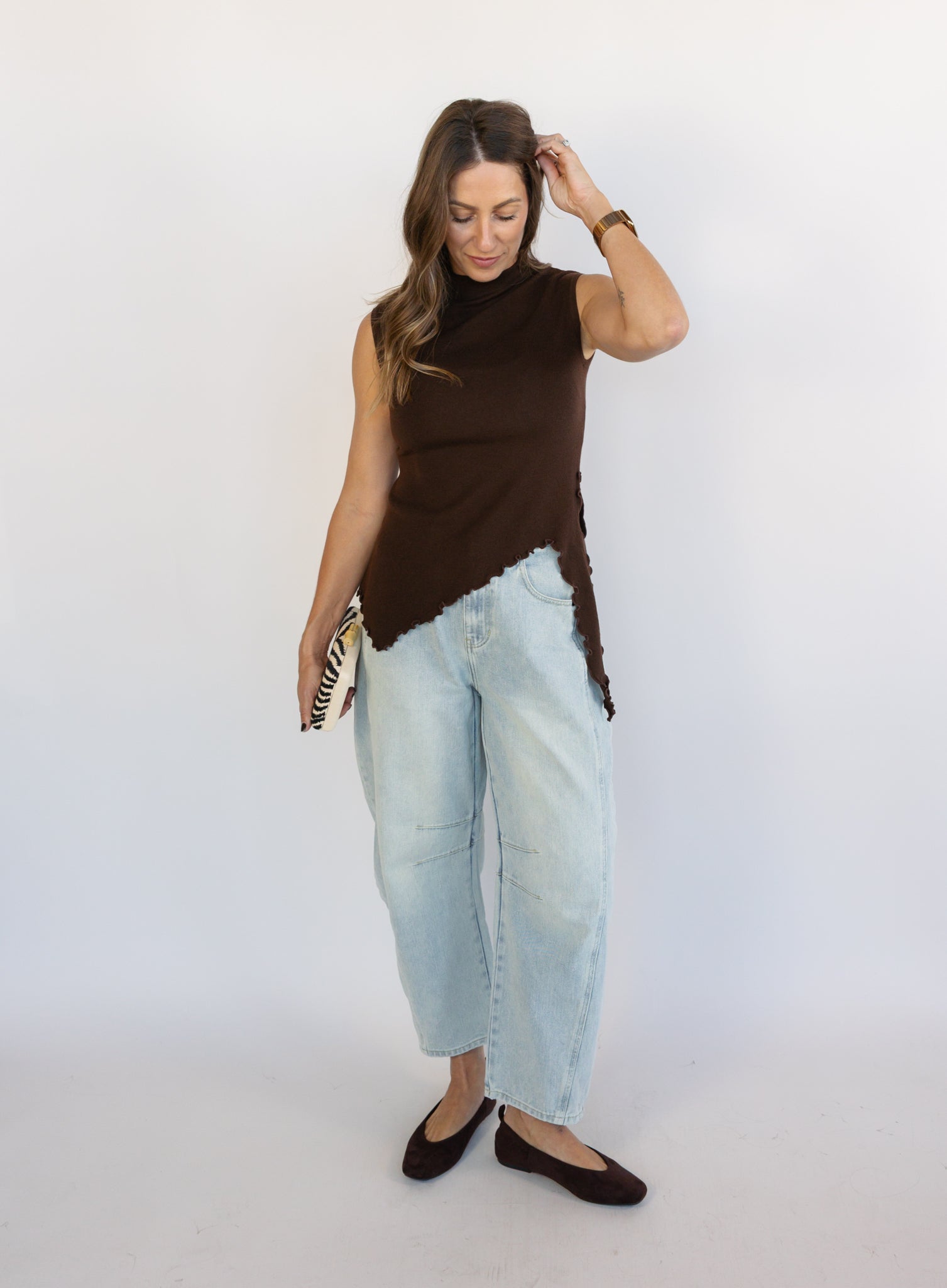 Woman wearing the Coralie Ruffle Trim Sweater Tank, a chocolate brown mock neck knit tank with a ruffle hem
