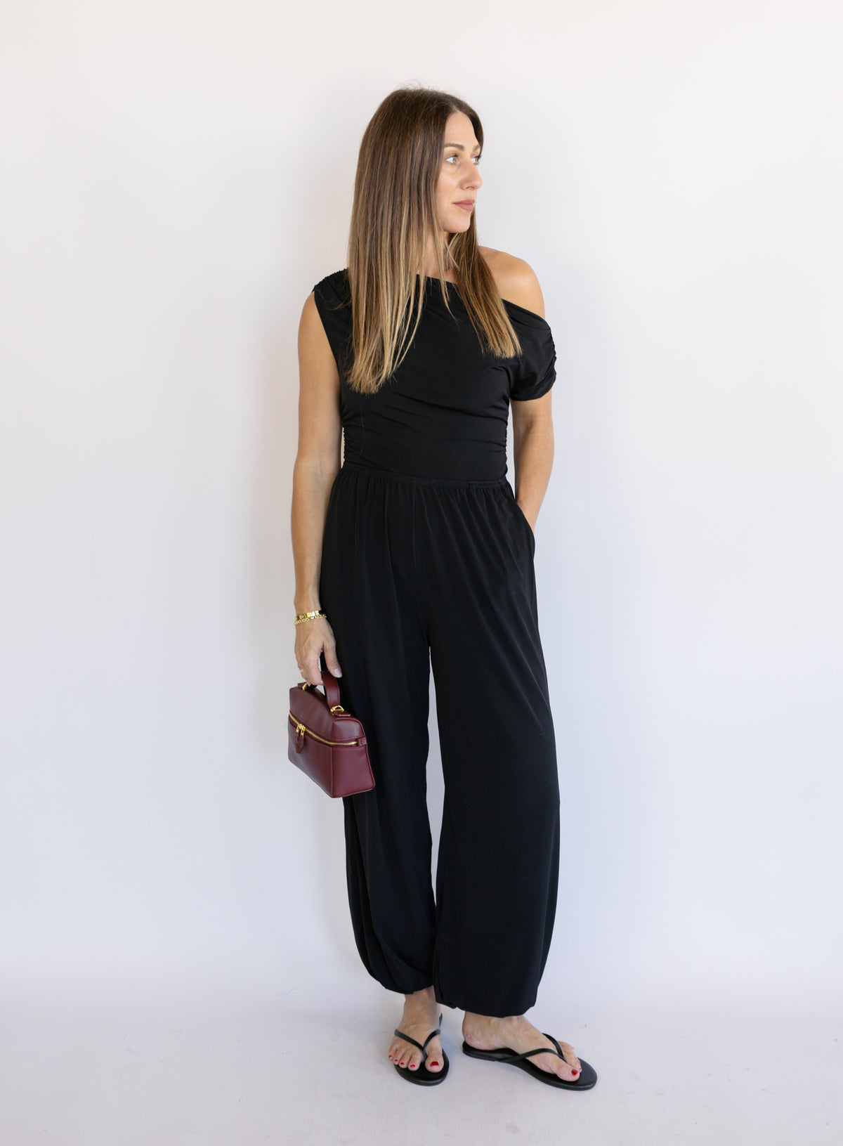 Woman wearing the Azalea One Shoulder Top, a black off-the-shoulder top with a cinched waist