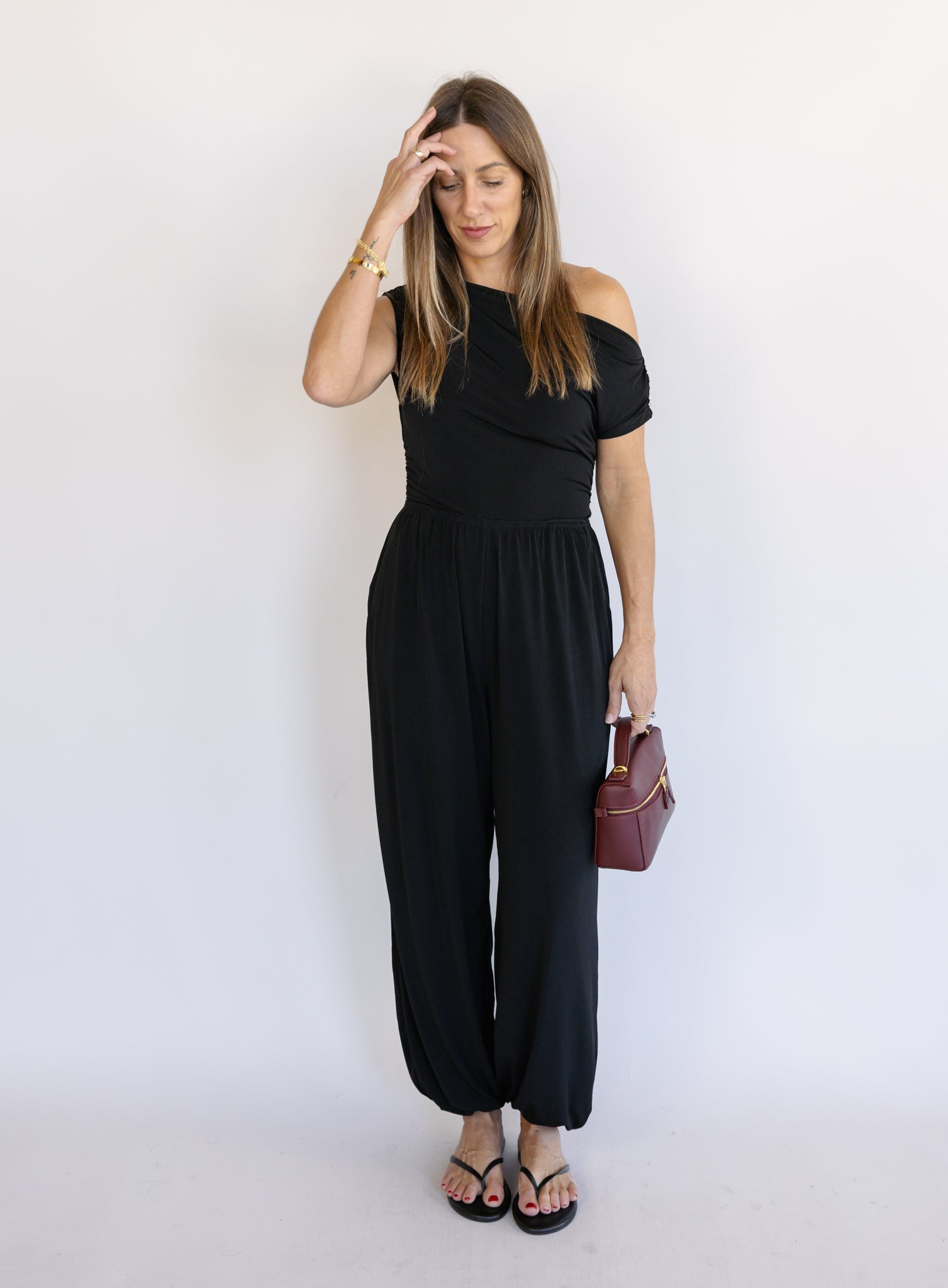 Woman wearing the Azalea One Shoulder Top, a black off-the-shoulder top with a cinched waist