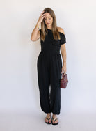 Woman wearing the Azalea One Shoulder Top, a black off-the-shoulder top with a cinched waist