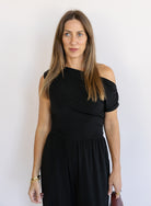 Woman wearing the Azalea One Shoulder Top, a black off-the-shoulder top with a cinched waist