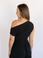 Woman wearing the Azalea One Shoulder Top, a black off-the-shoulder top with a cinched waist